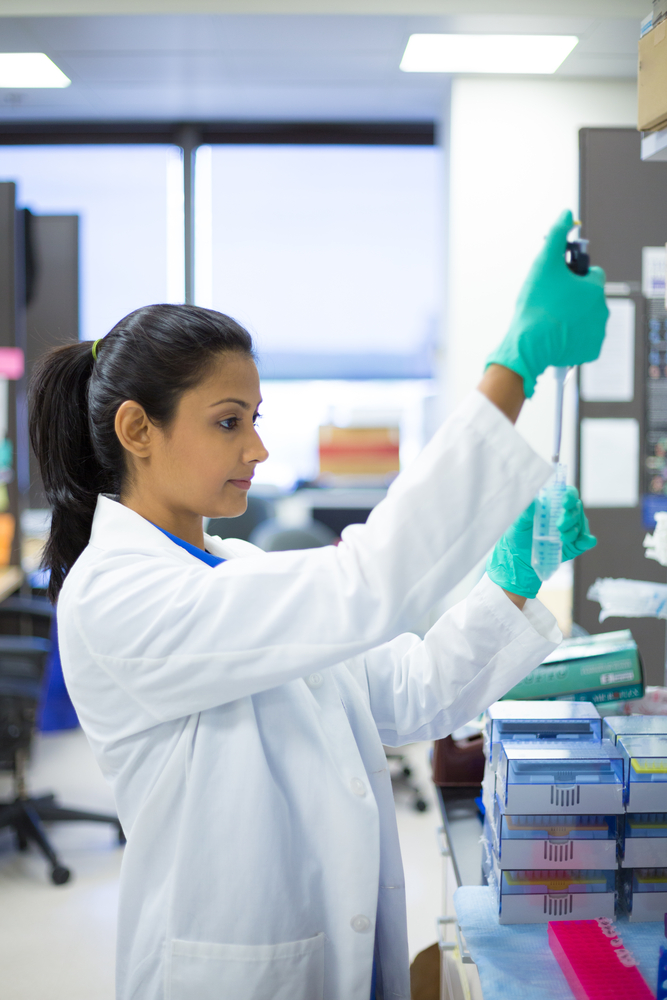 A woman in lab coat and gloves working with equipment.